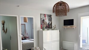 Ein modernes, helles Zimmer mit Esstisch, Stühlen, Fernseher und einem Bett, das mit einer Segelboot-Dekoration versehen ist.