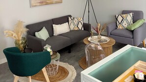 Ein modernes Wohnzimmer mit grauem Sofa, einem grünen Sessel, einem Couchtisch und einer dekorativen Stehlampe.