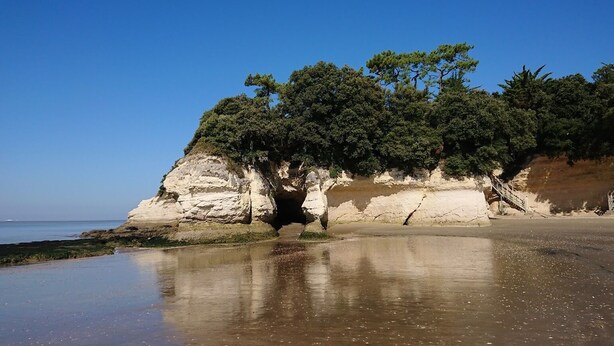Eine Küstenlandschaft mit Sandstrand, Felsenklippe und blauem Himmel.