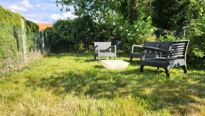 Un espacio al aire libre con césped, dos bancos y una mesa blanca.