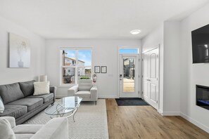 A modern living room with a gray sofa, a glass coffee table, a white armchair, and a fireplace.