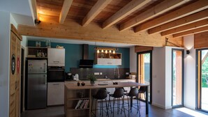 Une cuisine moderne avec des poutres en bois, un îlot central doté de tabourets de bar et une grande fenêtre qui laisse entrer la lumière naturelle.