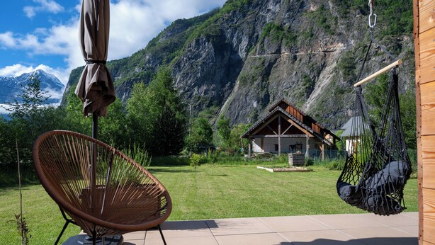 Une terrasse avec une chaise, un fauteuil suspendu et une maison avec une vue sur les montagnes en arrière-plan.