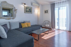 Ein Wohnzimmer mit grauem Sofa, einem kleinen Tisch, einem Sessel und einer Steinwand mit einem Bild.