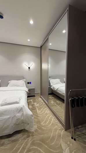 Una camera d'albergo con un grande specchio, due letti, un comodino e una lampada fissata al muro.