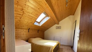 Un dormitorio con techo inclinado, tragaluz, cama, radiador y una puerta.