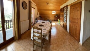 Un comedor con techo de madera, una mesa redonda con sillas, un reloj en la pared y vistas a través de un ventanal.