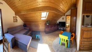 Una habitación estilo loft con techo de madera, un sofá, una mesa de comedor con sillas y una zona de cocina.