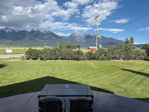 A patio with a table and chairs, a mountain view, and a red barn in the background.