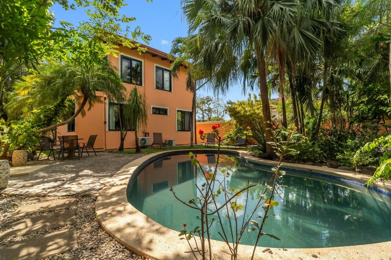 Ein Pool mit geschwungener Kante, umgeben von einer Terrasse mit Stühlen und einem Tisch.