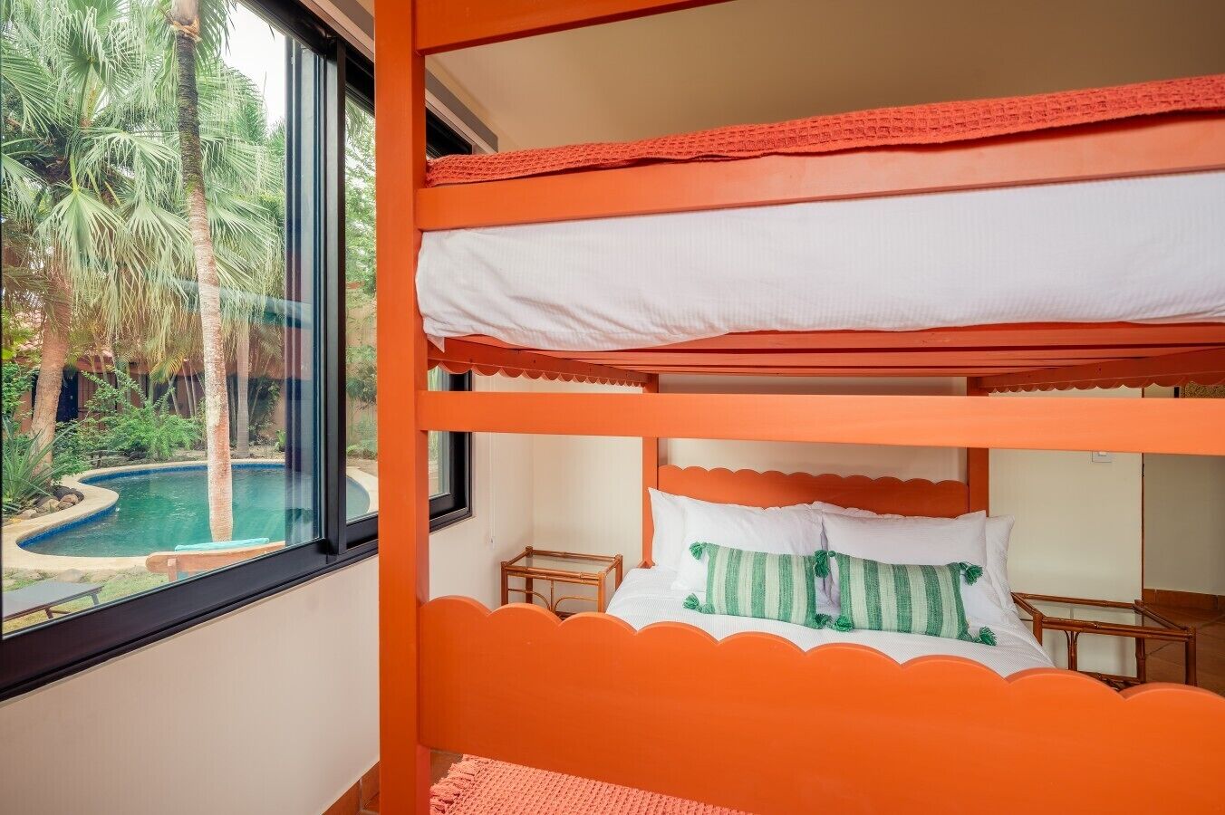 Une chambre avec des lits superposés donnant sur une piscine et des palmiers.