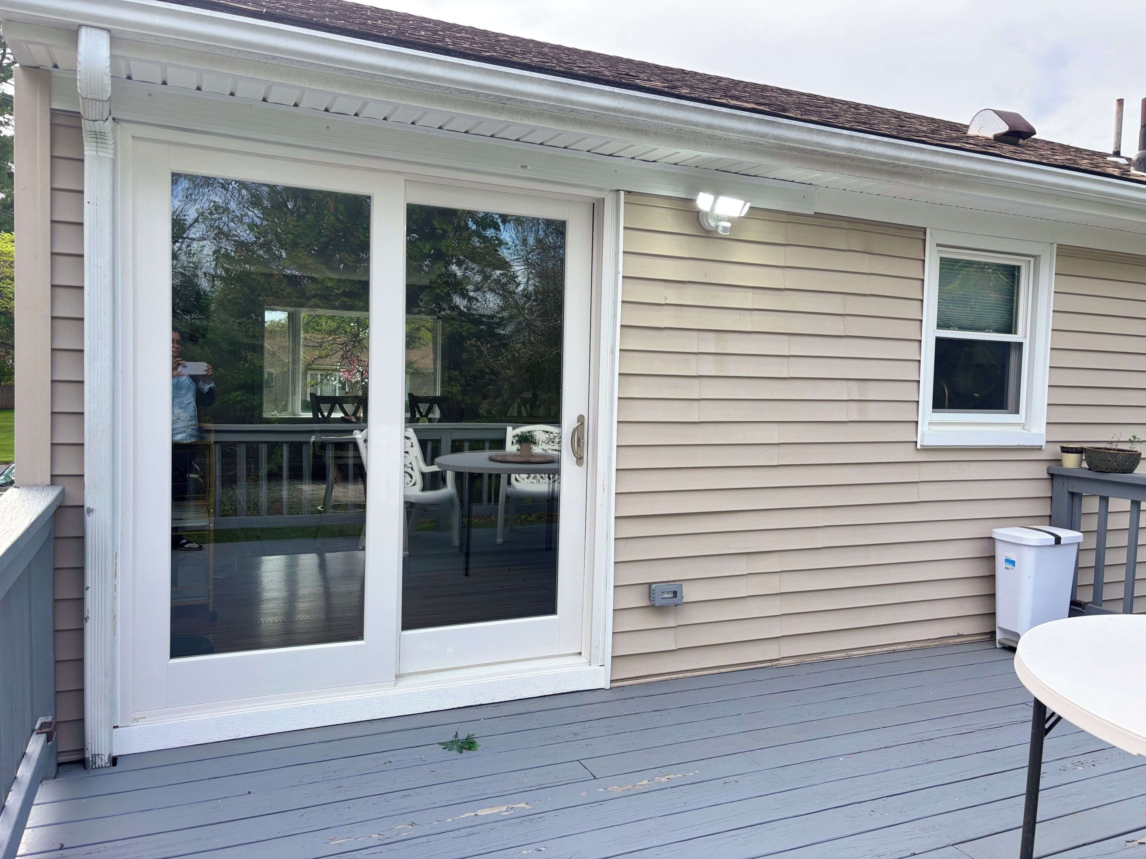 A house with a sliding glass door leading to a deck, a small window, and a trash can.