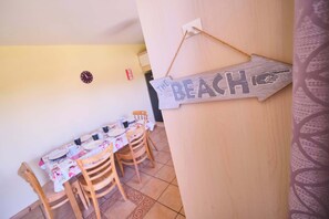 Zona pranzo con tavolo imbandito per quattro persone, sedie in legno e orologio a parete.