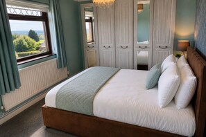 Ein Schlafzimmer mit Bett, einem Vorhangfenster, einem Heizkörper und Blick ins Grüne.