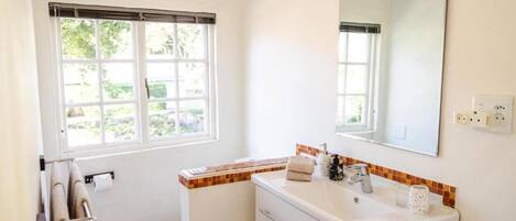 A bathroom with a toilet, sink, mirror, towel rack, and a window.