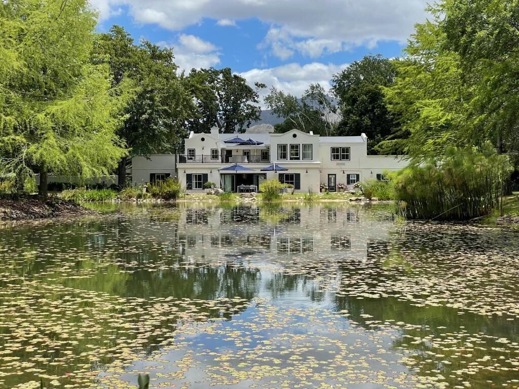 A large, two-story building with a symmetrical facade, a covered patio area, and a pond with lily pads in front.
