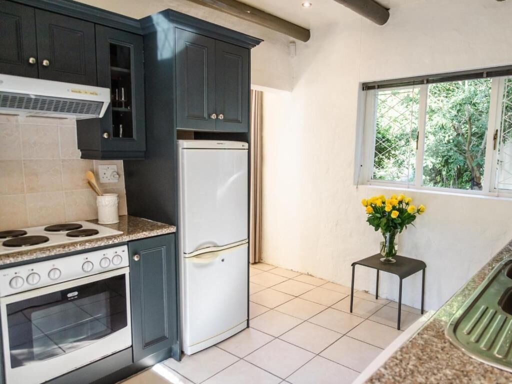 A kitchen with dark cabinets, a white refrigerator, a stove, and a window with a view of greenery.
