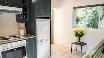 A kitchen with dark cabinets, a white refrigerator, a stove, and a window with a view of greenery.