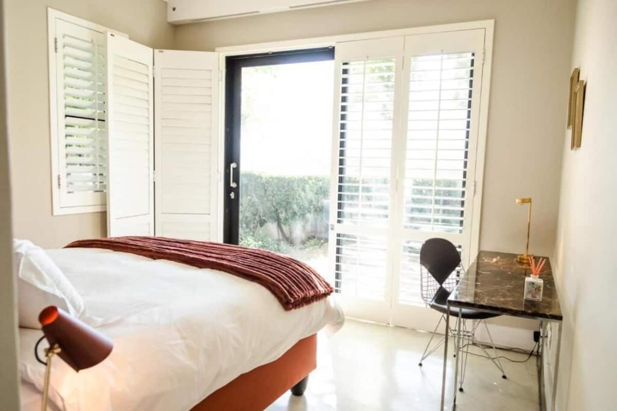 Un dormitorio con cama, escritorio y puerta que da a un espacio exterior.