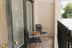 Una puerta con diseño de malla metálica, dos sillas de mimbre y una pared blanca.