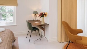 A hotel room with a bed, a desk with a chair, a lamp, a vase with flowers, and a window with a view of trees. - Klein Champagne Guesthouse and Cottages (Franschhoek)