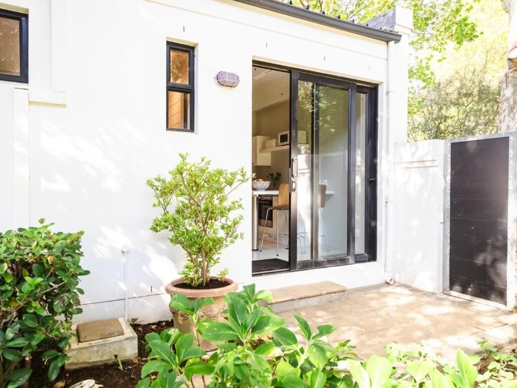 A modern house with a sliding glass door, a small garden with potted plants, and a visible kitchen area.