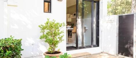 A modern house with a sliding glass door, a small garden with potted plants, and a visible kitchen area.
