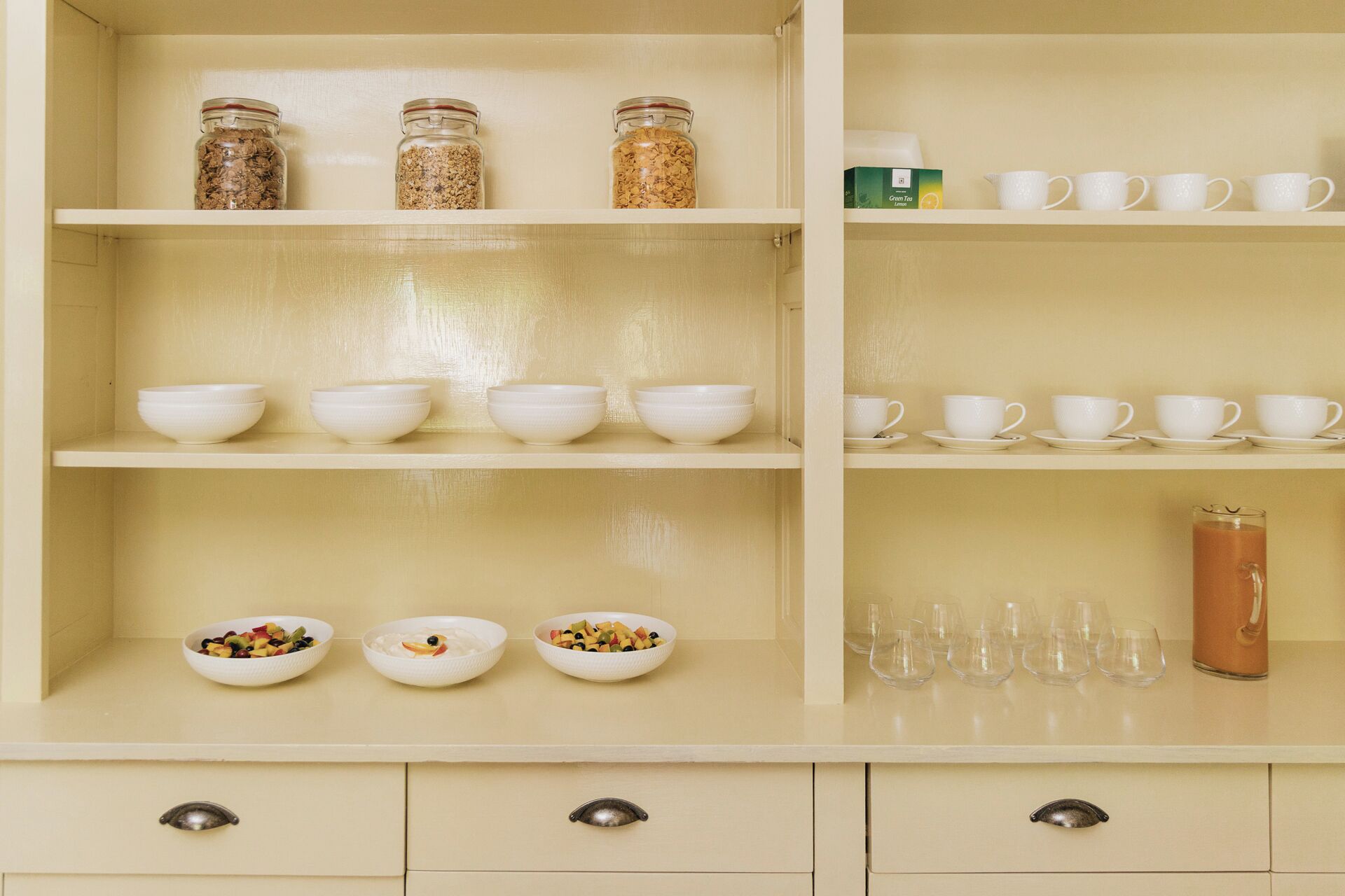 A kitchen with three shelves, each holding bowls, jars, and cups.