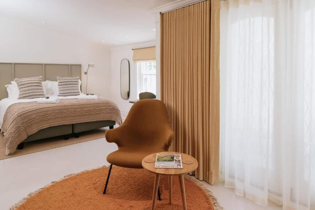 Un dormitorio con cama, una silla, una mesita y una ventana con cortinas.