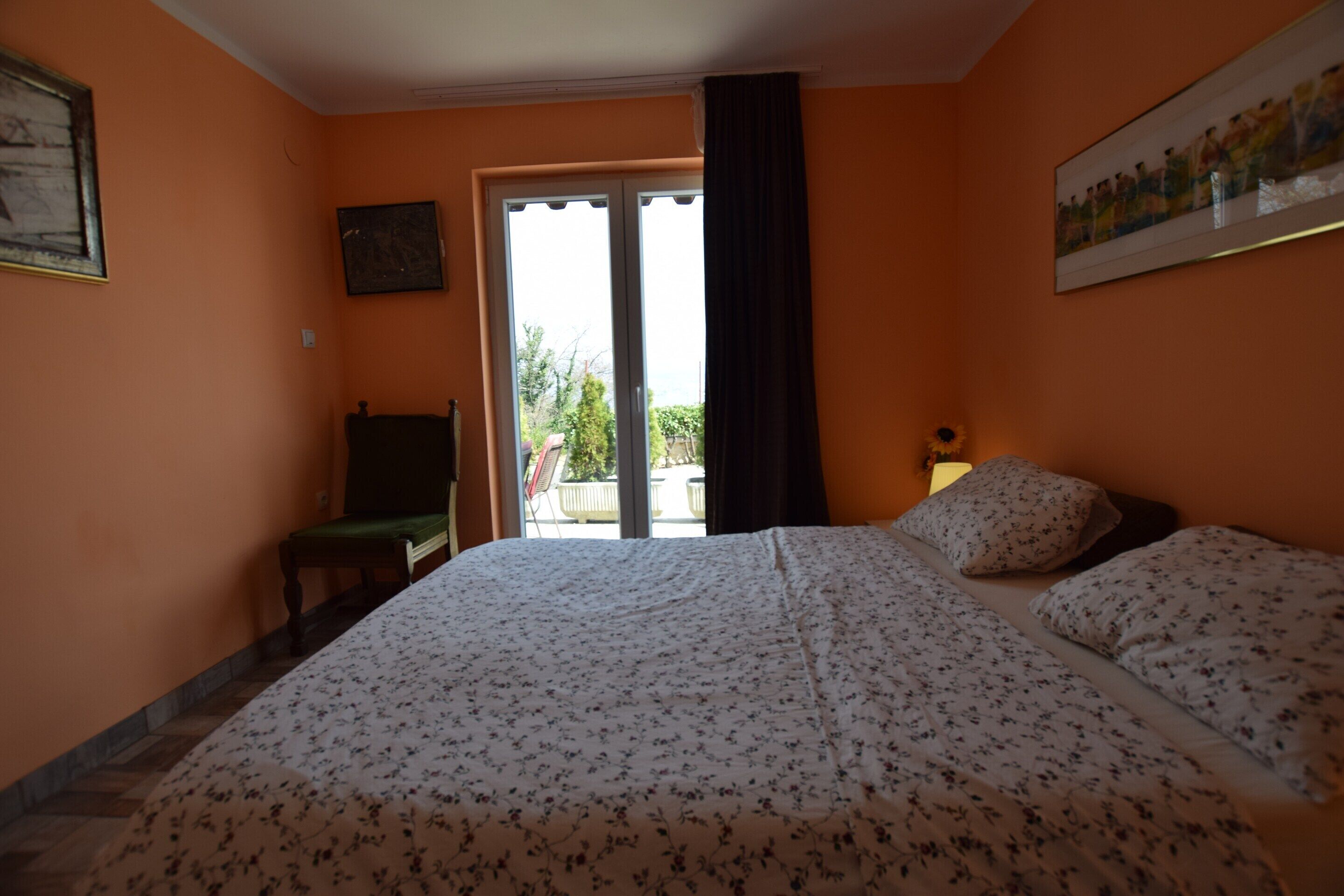 A bedroom with a bed, a chair, a desk, a window with curtains, and a painting on the wall.