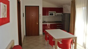 A compact kitchen with a microwave, refrigerator, and a dining area with red chairs. - Comfortable Flat 80m From the sea (San Michele al Tagliamento)