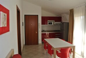 Eine kompakte Küche mit Mikrowelle, Kühlschrank und einem Essbereich mit roten Stühlen.
