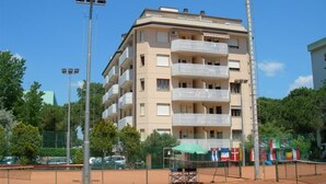 A multi-story building with balconies, a tennis court, and a tall pole. - Comfortable Flat 80m From the sea (San Michele al Tagliamento)