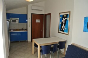 A compact kitchen with blue cabinets, a microwave, and a dining area with a table and chairs. - Cozy Stay 80m From the Beach (San Michele al Tagliamento)