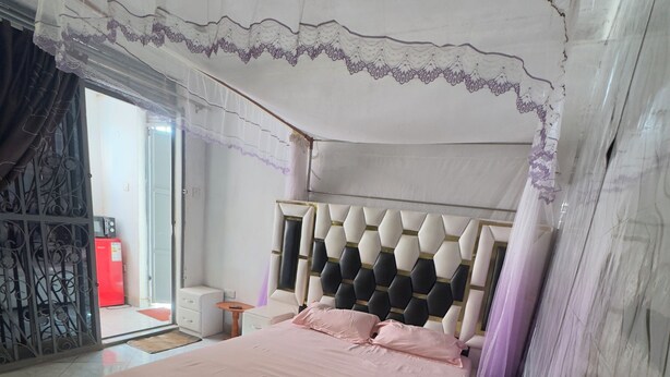 Ein Schlafzimmer mit einem Bett, einem Nachttisch, einem roten Gerät und Blick ins Freie.