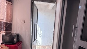Ein Zimmer mit Fliesenboden, einem roten Schrank, einem Korbsessel, einer Mikrowelle und einer Schiebetür zum Außenbereich.