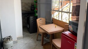 Eine kleine Küche mit Esstisch, Stühlen, einem Kühlschrank und einer Gasflasche.
