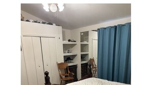 A bedroom with a bed, a wardrobe, a chair, and a shelf with various items. - Cancer patients that need peace, quiet, support & proximity to treatment plans. (Cave Creek)