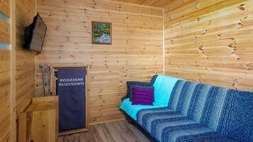 A wooden cabin interior with a sofa, a painting, and a sign reading 'RODZINNE RUSINOWO'.