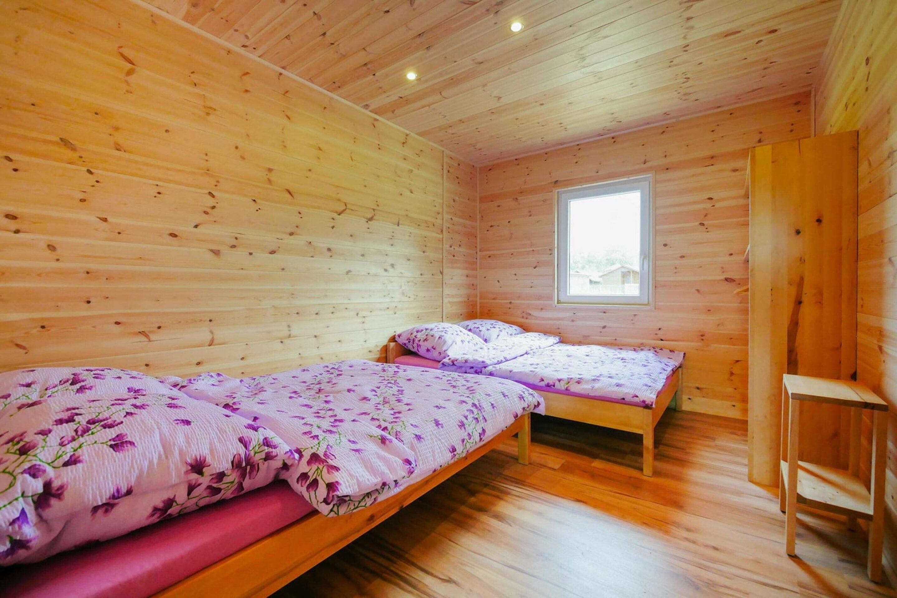 Eine Holzhütte mit zwei Betten, einem Fenster und einem Holzstuhl.