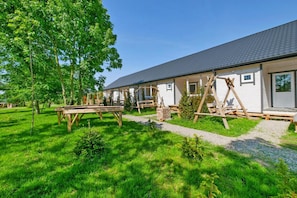 A row of white cabins with dark roofs, wooden benches, and a picnic table in a grassy area. - Holiday Homes, Attractions for Children (Postomino)