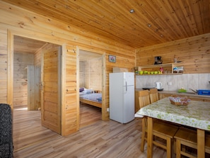 A wooden cabin with a kitchen, a dining area, and a bedroom with a bed and a refrigerator. - Holiday Homes, Attractions for Children (Postomino)