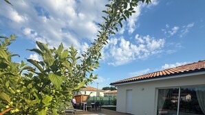 Una piscina con cubierta de madera, rodeada de follaje y un edificio con tejado de baldosas.