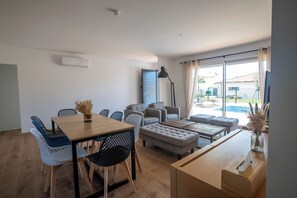 A modern living room with a dining table, sofas, and a large window. - CabGolf House - Premium golf house near the beach in Tosse, Landes (Tosse)