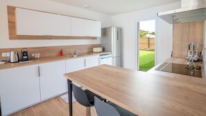 Una cocina moderna con armarios blancos, encimera de madera, refrigerador de acero inoxidable y vista a un césped verde.