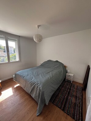 A bedroom with a bed, a nightstand, a lamp, a window, and a hanging light fixture. - Quiet apartment in Aubenas. 10 min walk from the Château. (Aubenas)