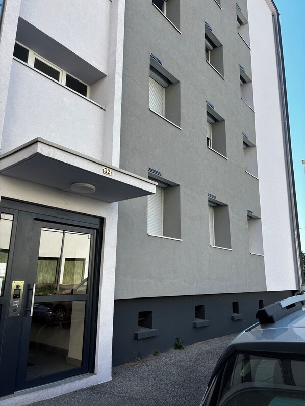 A modern building with a flat facade, numbered 32, featuring a ground-floor entrance with a glass door and a small parking area in front. - Quiet apartment in Aubenas. 10 min walk from the Château. (Aubenas)