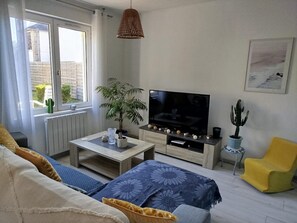 Un salon avec un canapé, un téléviseur, une table basse, une plante et un fauteuil jaune.