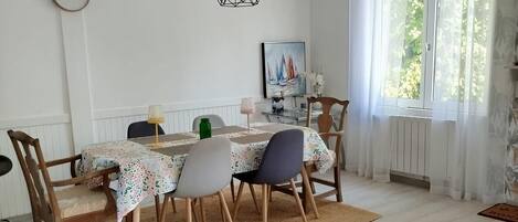 Een eetruimte met een tafel gedekt voor vier personen, een hanglamp, een klok aan de muur en een raam met gordijnen.