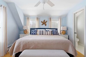 A bedroom with a bed, two bedside tables, a ceiling fan, a starfish decoration, and a window with blinds.
